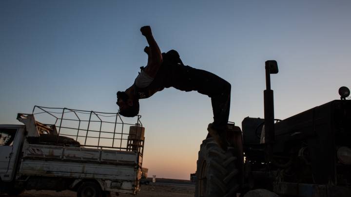 A fighter of the YPG doing a backflip from a vehicle.