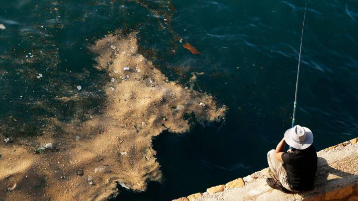 A fisherman in Beirut watches as dumped waste floats past his line.